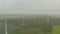 Aerial: view over foggy agricultural yellow field with multiple wind turbines generating power trough wind for a