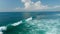 Aerial view of people surfing across the waves in tropical blue ocean. Fast wave breaking across the ocean surface