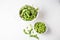 Aerial view of pods in drainer and edamame grains in white bowl, on white table, horizontal