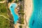 Aerial view of pool, umbrellas, sandy beach with green trees