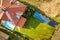 Aerial view of a private house with green grass covered yard, solar panels on roof, swimming pool with blue water and wind turbine