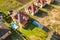 Aerial view of a private house with green grass covered yard, solar panels on roof, swimming pool with blue water and wind turbine