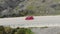 Aerial view of red car moving along road near sea. Passenger car drives along fortified straight road along azure sea