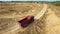 Aerial view of red dump truck moving on the sand road in a quarry near the forest in summer day. Scene. Industrial