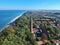 Aerial view at red lighthouse, at baltic sea coast with forest and buildings.