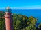 Aerial view at red lighthouse, at baltic sea coast with forest and buildings.