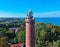 Aerial view at red lighthouse, at baltic sea coast with forest and buildings.