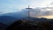 Aerial view of a religious Christian steel cross on a hill in the mountainous countryside, in sunset