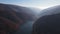 Aerial view of the reservoir among fir trees with the mountains range on the horizon, drone flies forwards over the dam