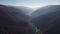 Aerial view of the river among fir trees with the mountains range on the horizon, drone flies forwards over the