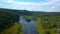 Aerial view of river and forest at summer day, sky and clouds. Clip. Flying over rippling river banks and green woodland