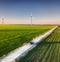 Aerial view of road on beautiful summer field at sunset. Landscape with rural road, wind power turbines. Road through the field. T