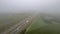 Aerial view of the road between farm fields and plantations under a grey misty sky, shot with a drone