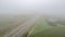 Aerial view of the road between farm fields and plantations under a grey misty sky, shot with a drone