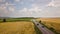 Aerial view of a road with moving cars between yellow agriculture wheat fields ready to be harvested in late summer.