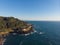 Aerial view of rock with green forest in the ocean. Blue water background. Sunny weather. Beauty of Earth. Wallpaper