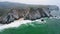 Aerial view of rocky cliff formation of Praia da Adraga beach, Portugal Atlantic coast. Cabo do Paco Lighthouse in