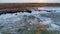 Aerial view of rocky coastline with crashing waves and herd of sheeps