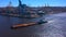 Aerial view of a row of construction or cargo cranes on the river bank with a barge passing by.