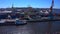 Aerial view of a row of construction or cargo cranes on the river bank with a barge passing by.