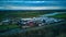 Aerial view of a rural landscape with farmland, a river, and clustered buildings under a cloudy sky at dusk