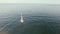 Aerial view of sail yacht sailing at sea near coastline. Blue sea with sun reflections. Drone view - birds eye angle.