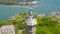 Aerial view sea light house on rocky island in blue sea and modern city on skyline. Drone view lighthouse tower on green