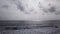 Aerial view of sea line waves, rocky coastaline and cloudy sky. Drone view of gray ocean and gloomy sky