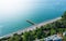 Aerial view of serene beach with long pier, azure waters, and vibrant beachgoers dotting shoreline