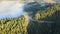 Aerial view of serpentine road between foggy green pine forest with canopies of spruce trees in autumn mountains.