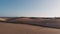 Aerial view is a side view of the dune along which a beautiful young woman walks. The golden hour at sunset or sunrise