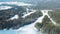 Aerial view of ski slope and people snowboarding on a ski track with coniferous trees from the both side of the track