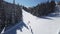 Aerial view of ski slope and skiers skiing down the slope during sunny day during winter holidays