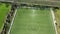 Aerial view of the slow overflight over an empty green football field with a view of agricultural field and meadow at the edge