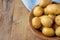 Aerial view of small yellow potatoes in wooden bowl, with selective focus, with blue checkered cloth, on rustic wooden table, hori