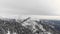 Aerial view of snow capped mountain range. Drone overview of snowy mountain, dark forest and moody weather. Scenic