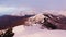 Aerial view of snow covered mountain range during pink and yellow sunset in autumn. Dark forest on the mountain slope