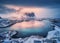 Aerial view of snowy mountain, village on sea coast, colorful sky