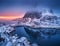 Aerial view of snowy mountain, village on sea coast, colorful sky