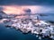 Aerial view of snowy mountain, village on sea coast, orange sky