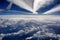 Aerial view of snowy mountains, clouds and plane trails, opposite the sunlight