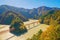 Aerial view of the steam train crossing Oigawa Railroad to go to station with red fall foliage in forest mountain hills and blue