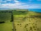 Aerial view of straight rural road passing through meadows and pastures on bright sunny day.