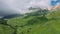 Aerial view of stunning mountain landscape under soaring clouds, casting shadow on green valley of mountainside