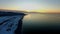 Aerial view of a stunning sunset with a coastline below along the shore of a large lake, sea or ocean
