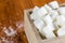 Aerial View of Sugar Cubes in Square Shaped Bowl and Spoon with Unrefined Sugar spill over in Wooden Background.