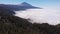 Aerial view - thick clouds cover the valley, pine forest and volcano. Tenerife, Spain