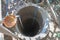 Aerial view to the depth of a well. Deep well made of concrete rings with blue rope and orange bucket filled with water.