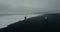 Aerial view to the young couple on the black volcanic beach in Iceland. Man runs from the wave on the shore, woman waits