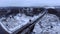 Aerial view tracking from a drone behind a railway train moving on a bridge over a freezing river.